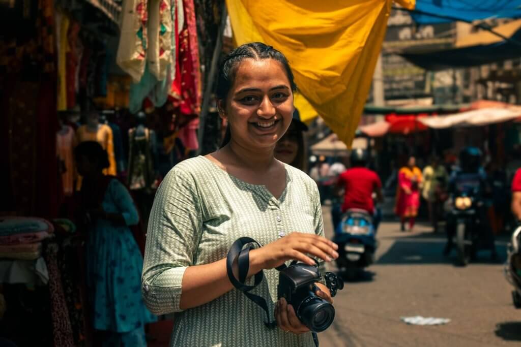 Smiling woman holding a camera in the bustling streets of Jalandhar, India.